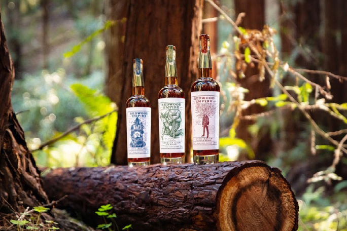 Three Redwood Empire whisky bottles on top of a cut tree in forest
